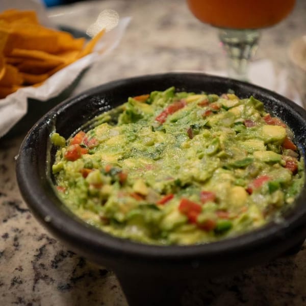 A black bowl of chunky guacamole with diced tomatoes and onions, next to tortilla chips.