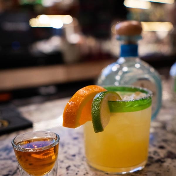 A margarita with orange and lime slices, a shot of tequila, and a tequila bottle.
