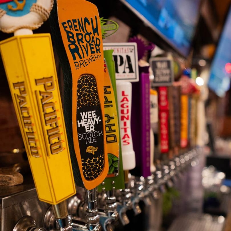 Close-up of a row of colorful beer taps, including Pacifico and French Broad River Brewery.