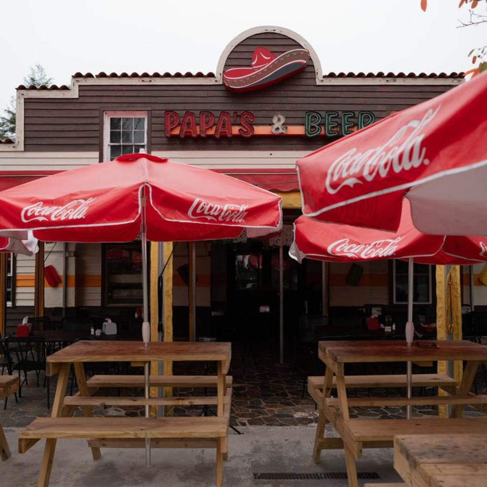 Papa's & Beer restaurant exterior with red Coca-Cola umbrellas and wooden picnic tables.
