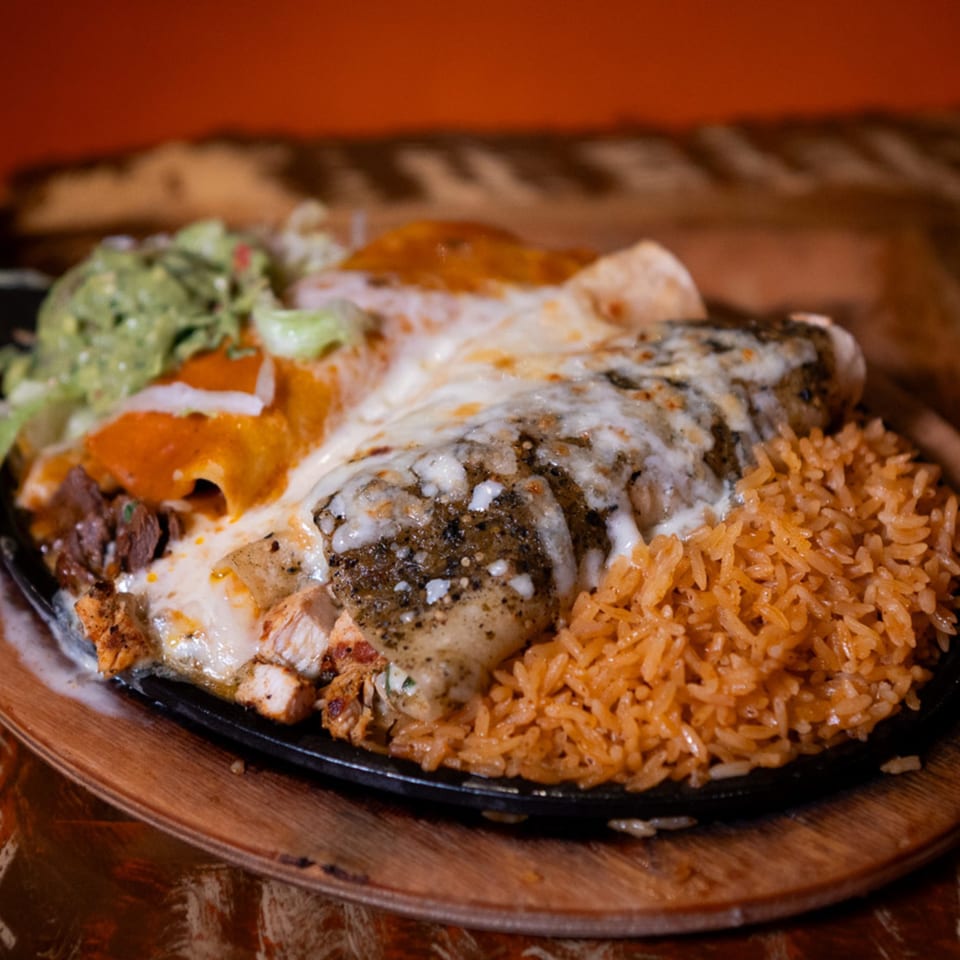 Sizzling fajita platter with chicken, steak, melted cheese, guacamole, and rice at Papa's & Beer.