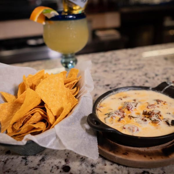 Margarita, a basket of tortilla chips, and a skillet of queso fundido on a counter.