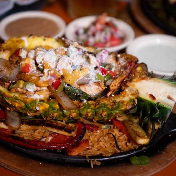 A pineapple half filled with fajita-style chicken, peppers, onions, and cheese, served with rice.
