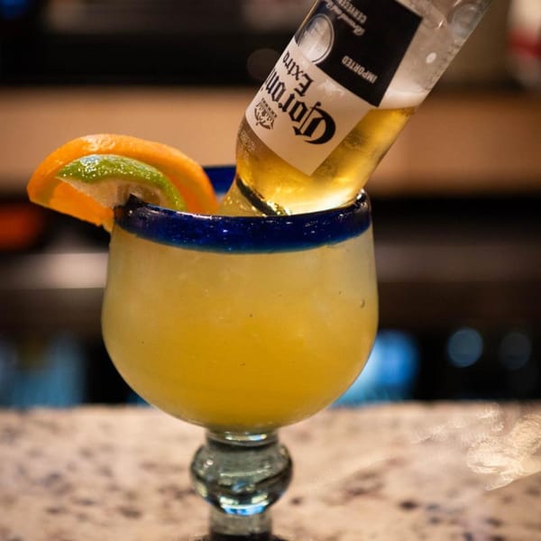 A Corona beer bottle inverted into a large margarita glass with orange and lime slices.