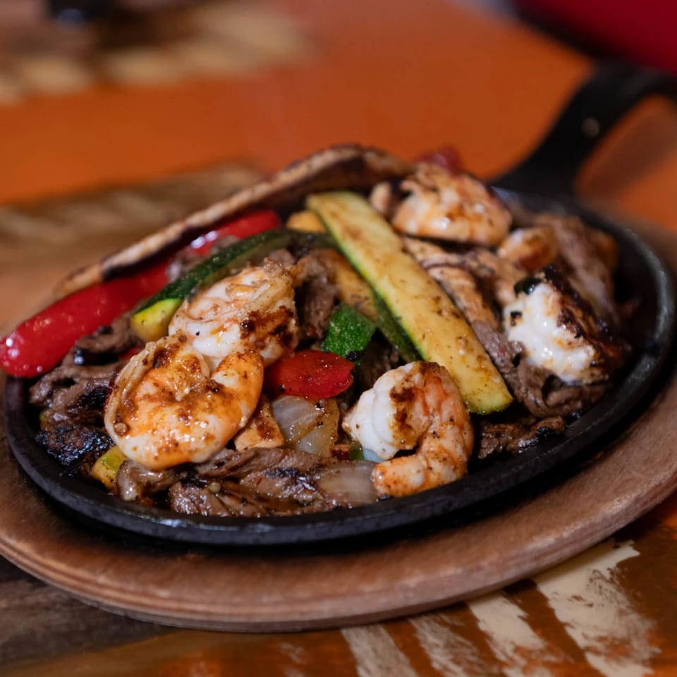 Sizzling fajitas with shrimp, steak, red peppers, and zucchini in a cast iron skillet.