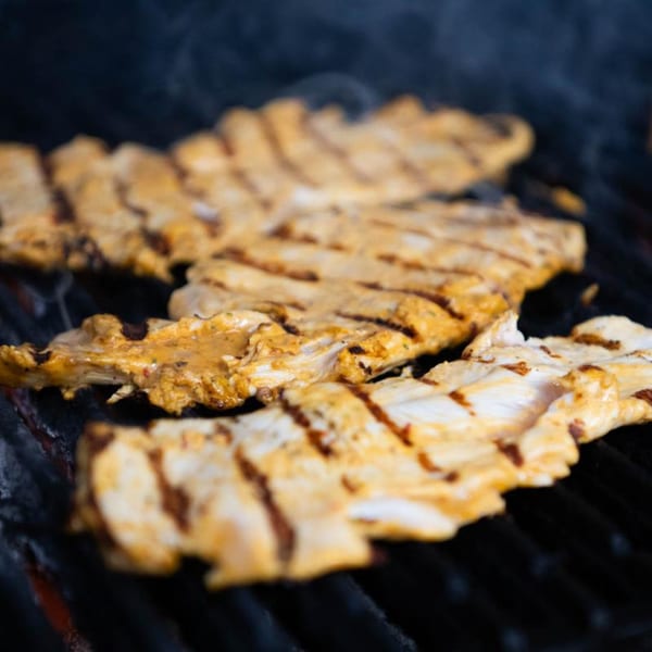 Marinated chicken cooking on a grill with visible grill marks and smoke rising.