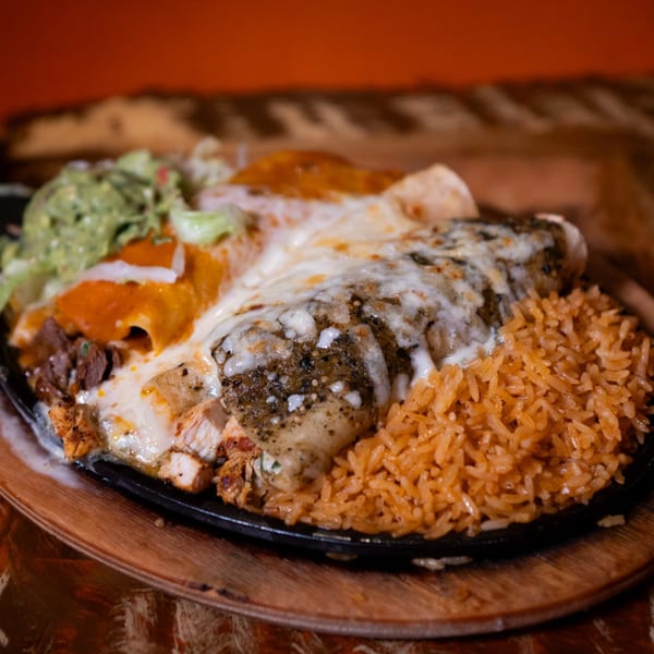 Sizzling Mexican fajitas with chicken, steak, rice, guacamole, and cheese on a hot plate.